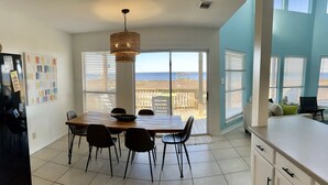 Een moderne keuken met een eettafel en stoelen, een koelkast en uitzicht op de oceaan door grote ramen.