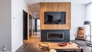 A modern living room with a fireplace, a mounted TV, and a wooden accent wall. - Tremblant Prestige - Horizon 1-104 (Mont-Tremblant)