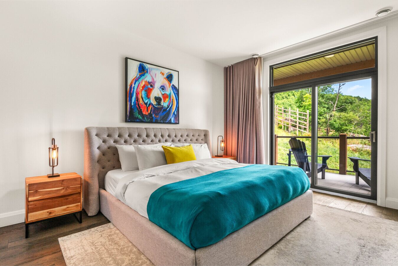 A bedroom with a large bed, a nightstand, a painting, and a view of the outdoors.