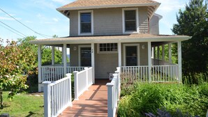 A two-story house with a porch, white railings, and a brick chimney.