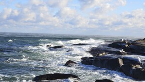 A rocky shoreline with waves crashing against the rocks under a partly cloudy sky.
