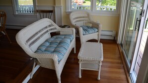 A room with wicker furniture, including a sofa and two chairs, near a window with a view of a garden.