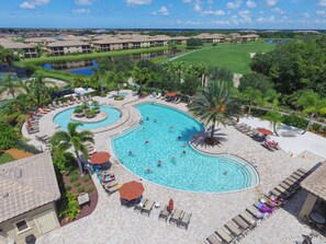 A large, multi-lane swimming pool with lounge areas and palm trees, surrounded by a residential complex.