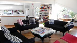 Ein modernes Wohnzimmer mit schwarzen Sofas, einem Couchtisch mit Zeitschriften und einer Küche im Hintergrund.