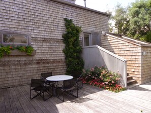 Eine Holzterrasse mit rundem Tisch und Stühlen, ein kleiner Garten mit Blumen und ein Holzzaun.
