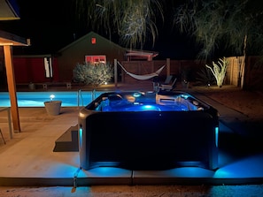 A hot tub with blue lighting, a pool, a hammock, and a house in the background.
