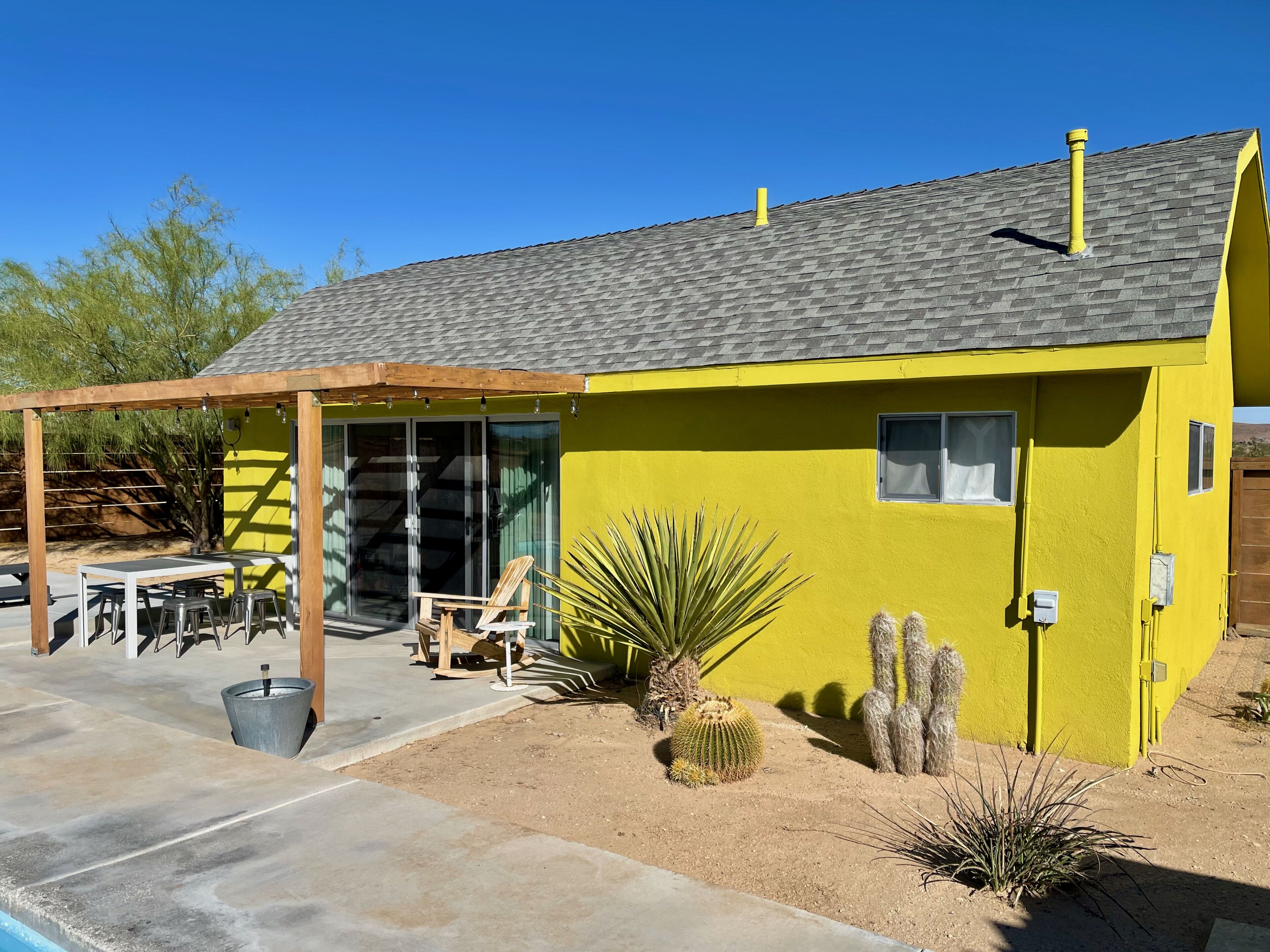 Una casa amarilla con patio, piscina y plantas desérticas.