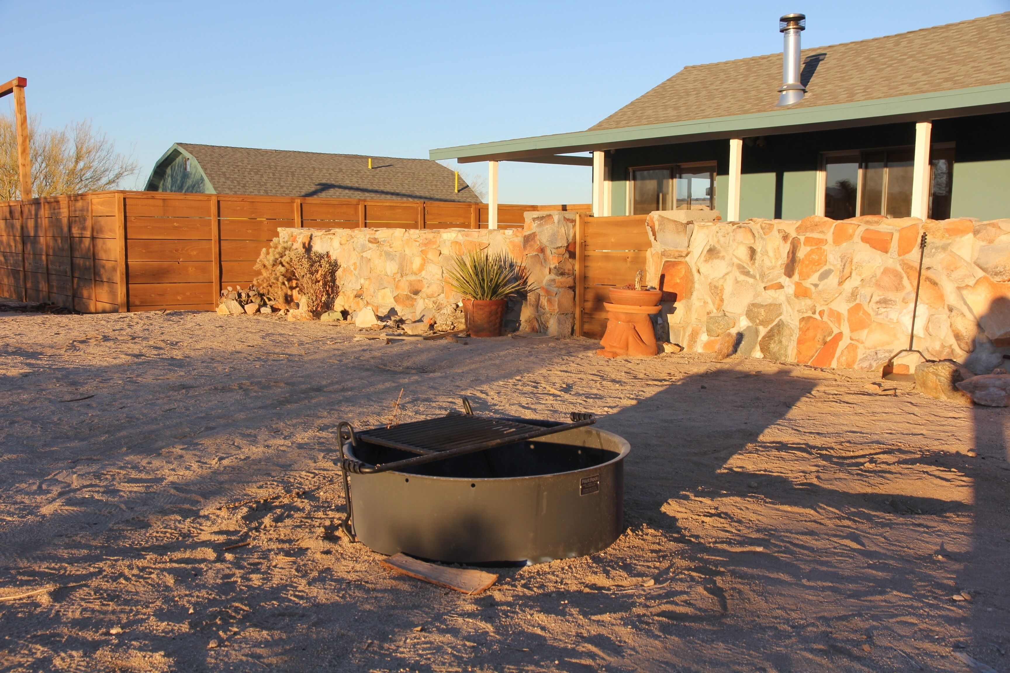 A sandy outdoor area with a large metal pot and a wooden bench.