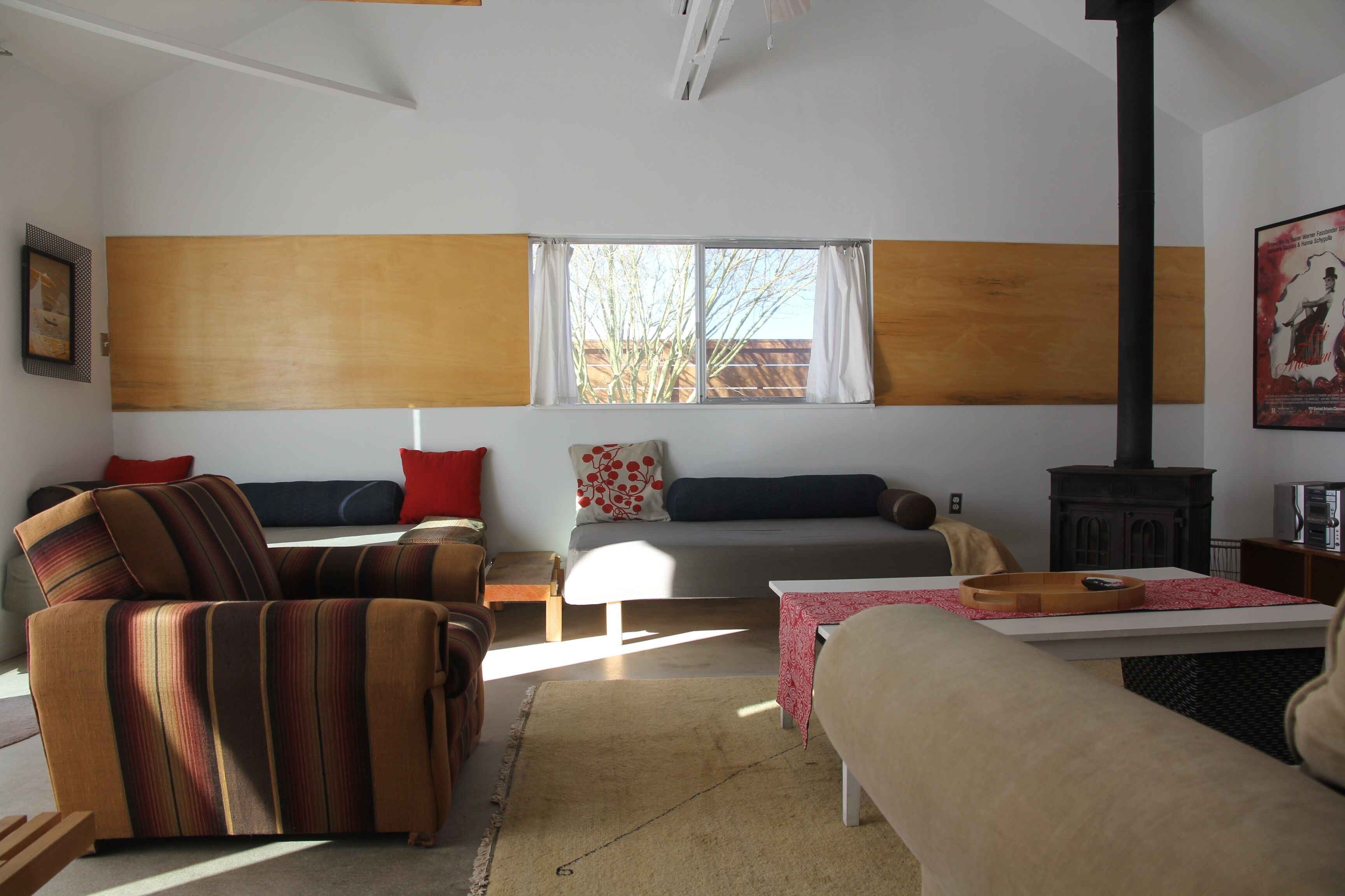 Un salon comprenant un canapé, un fauteuil et une table avec un plateau. Il y a une fenêtre avec des rideaux et une cheminée.