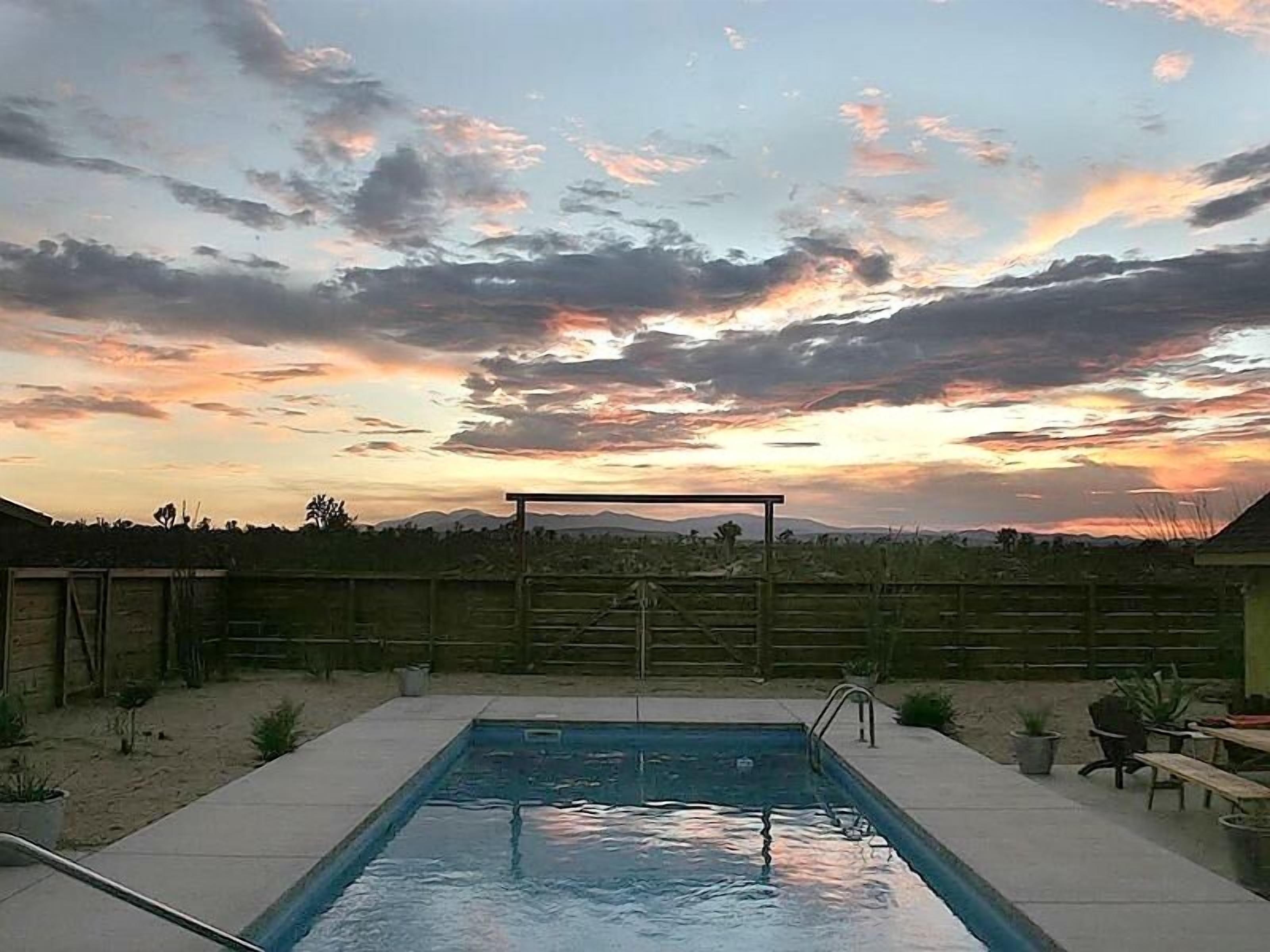 A backyard with a swimming pool, a wooden fence, and a view of the sunset.