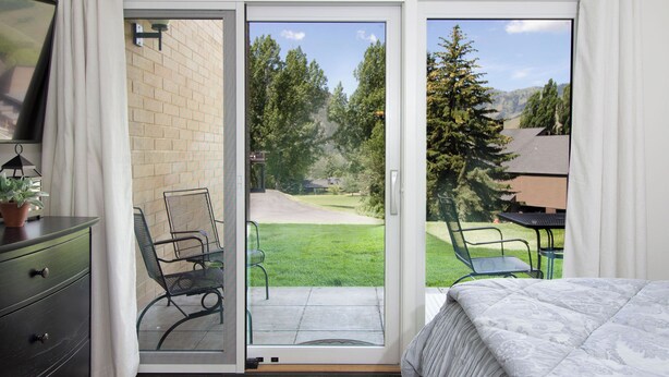 Quarto com porta de correr de vidro que dá para um pátio com gramado e uma mesa.