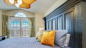A bedroom with a large bed, a dark wooden headboard, and a view of the outdoors through a window. - Spacious 4BR w/ EV Charger & Hot Tub (Colorado Springs)