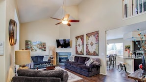 A modern living room with a dark-colored sofa, a coffee table, a TV, and artwork on the walls. - Spacious 4BR w/ EV Charger & Hot Tub (Colorado Springs)