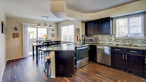 A modern kitchen with dark cabinets, a central island, stainless steel appliances, and a large window providing natural light. - Spacious 4BR w/ EV Charger & Hot Tub (Colorado Springs)