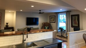 A modern kitchen with a built-in island, a flat-screen TV mounted on the wall, and a ceiling fan.