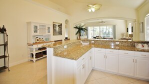 A spacious kitchen with white cabinetry, granite countertops, and a large island. - Large Private Pool Home-Walk/Bike to Beach & Mercato Shops & Dining (Naples)