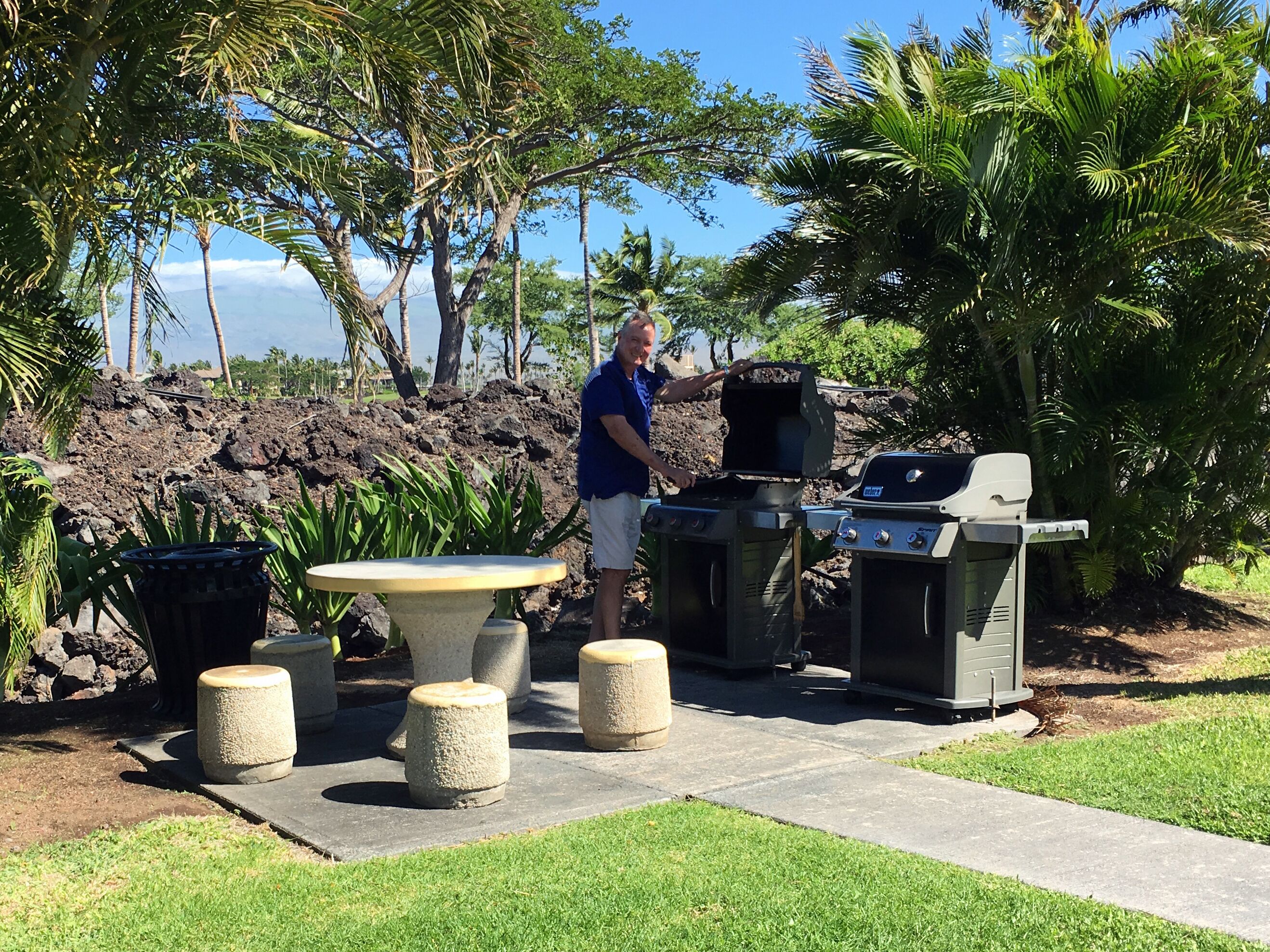 An outdoor grill area with two grills, a round table, and stone stools.