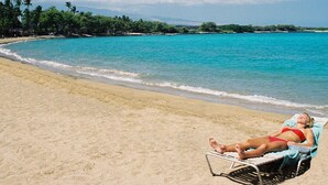 A beach with clear turquoise water, a sandy shore, and a person relaxing on a beach chair. - Last Minute Sale 50% off. Relaxing, remodeled end unit 601. Great view & 95 golf (Waikoloa)