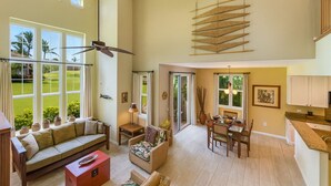 A spacious living area with a large window overlooking a green landscape, a dining area with a table and chairs, and a kitchen with white cabinets. - Last Minute Sale 50% off. Relaxing, remodeled end unit 601. Great view & 95 golf (Waikoloa)
