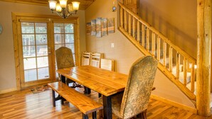 Une table à manger en bois avec des bancs, un escalier avec des rampes en bois et un lustre.