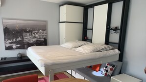 A modern bedroom with a bed, a desk, a chair, a round table, and a view of a cityscape. - Modern Cozy Studio in the heart of Paris (Paris)