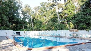Une piscine dotée d’une terrasse carrelée, entourée de chaises longues et d’une clôture blanche.