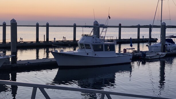 Un port de plaisance avec des bateaux amarrés à un quai, au coucher du soleil.