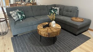 Ein modernes Wohnzimmer mit einem grauen Ecksofa, einem Holztisch und einem Essbereich mit Holzschränken und einer Kronleuchter.
