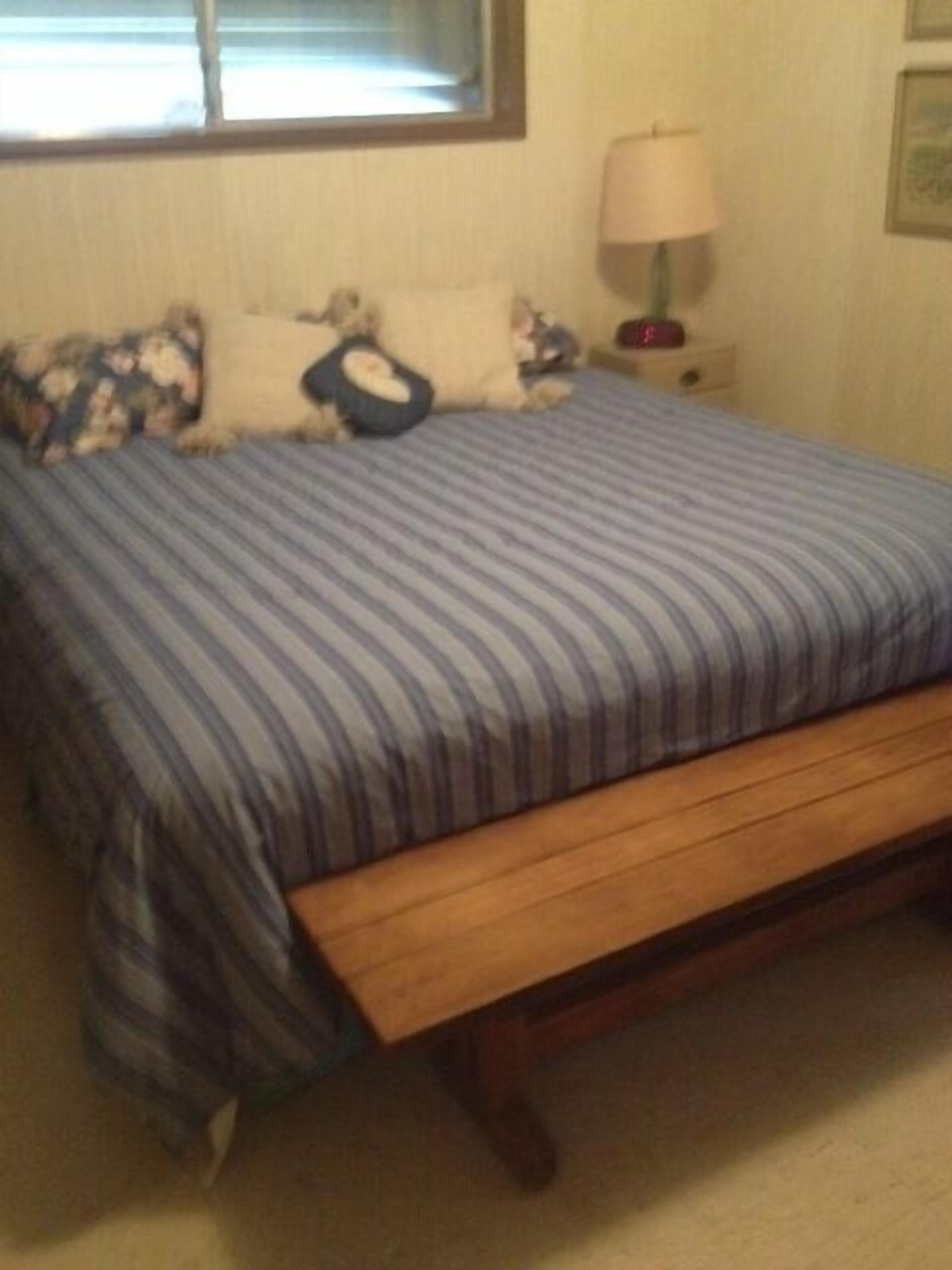 Un dormitorio con cama, almohadas, una mesita de noche y una lámpara.