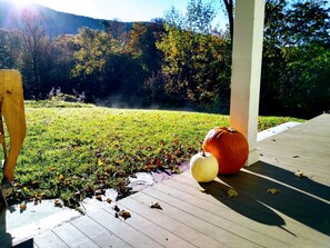 A porch with a wooden bench and two pumpkins on the floor.