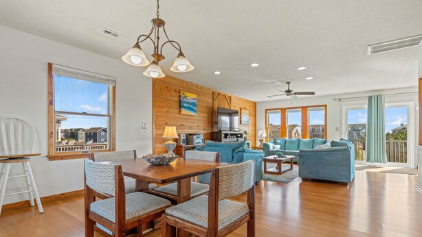 A spacious living room with a wooden floor, a dining area with a table and chairs, a blue sofa, and a television. - 4 Bedroom in Duck - Almost Oceanfront - Awesome views
 (Duck)
