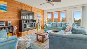 A living room with a wooden wall, a ceiling fan, a TV, a fireplace, a sofa, and a coffee table. - 4 Bedroom in Duck - Almost Oceanfront - Awesome views
 (Duck)