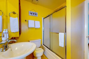 A bathroom with a yellow wall, a white sink, a toilet, and a glass-enclosed shower. - Boat Parking, In Town, Pet Friendly, Golf Cart Access (Port Aransas)