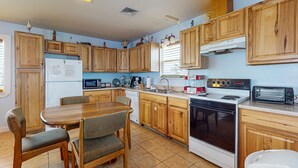 A kitchen with wooden cabinets, a dining table with chairs, a refrigerator, a microwave, a stove, and a toaster. - Boat Parking, In Town, Pet Friendly, Golf Cart Access (Port Aransas)