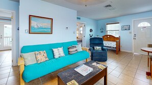 A living room with a turquoise sofa, a wooden coffee table, a blue armchair, and a wooden dining table. - Boat Parking, In Town, Pet Friendly, Golf Cart Access (Port Aransas)