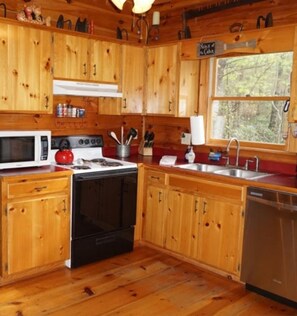 Enjoy cooking in this kitchen with a central island, microwave, stove, and dishwasher, offering a view of the surrounding forest.