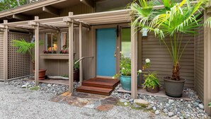A house with a blue door, wooden pergola, and potted plants.