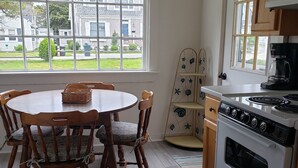 A kitchen with a dining table, chairs, a chandelier, a stove, and a view of the neighborhood through large windows.