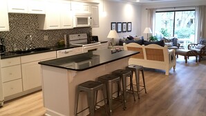 A modern kitchen with white cabinets, a black countertop, and a central island with stools.