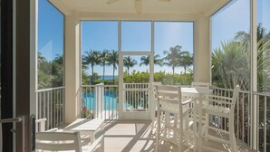 Ein sonniger Balkon mit weißer Möbel, einem Pool und Palmen im Hintergrund.