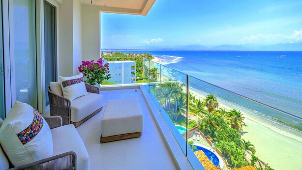 A balcony with a ceiling fan, a sofa with cushions, and a view of the ocean and beach.