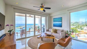 A spacious living room with a large window overlooking a scenic ocean view, a ceiling fan, and a modern interior design.