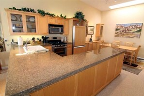 A kitchen with granite countertops, wooden cabinets, stainless steel appliances, and a dining area with a table and chairs. - Surf Song Condo, Pool, Spa & Whale Watching (Depoe Bay)