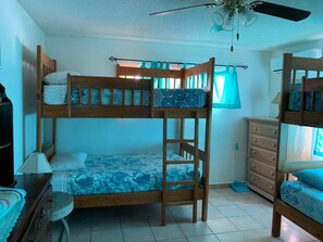 A bunk bed room with a ceiling fan, a dresser, and a window with curtains.