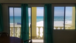 A room with a view of the beach through large windows with green curtains.