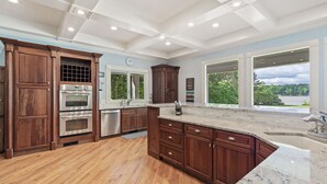A spacious kitchen with wooden cabinets, stainless steel appliances, and large windows offering a view of the outdoors. - Lakefront/8 Acres/Views/Families/Pool Table/Fire Pit/Kayaks/SUP/Quiet/HotTub (Greensboro)