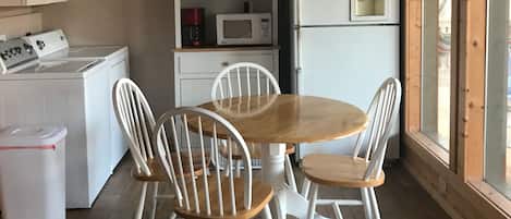 Cocina compacta con microondas, refrigerador y lavadora. Hay una mesa de comedor con cuatro sillas y un ventilador de techo.
