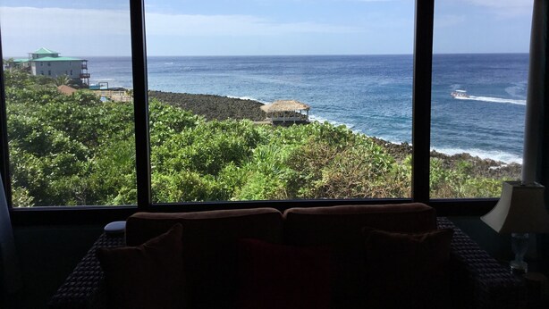 A room with a large window overlooking a coastal area with vegetation and a building. -  Location with spectacular views and six minute walk to the beach!!!  (Roatan)