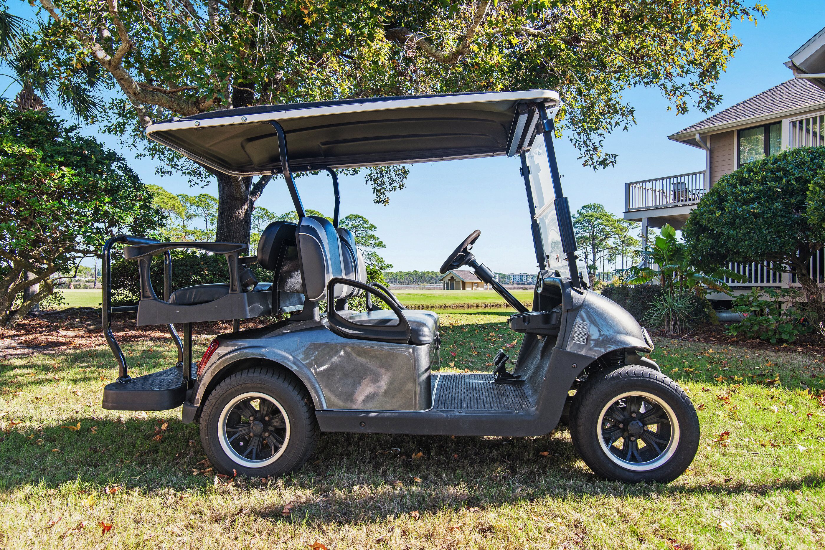 A golf cart parked on grass with a house and trees in the background.