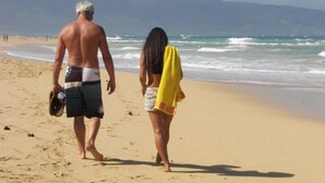 Una pareja caminando sobre una playa arenosa con olas del océano al fondo.
